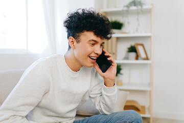 smiling young man talking on mobile phone, casual home interior, cozy setting with natural light, white and neutral colors, joyful communication concept