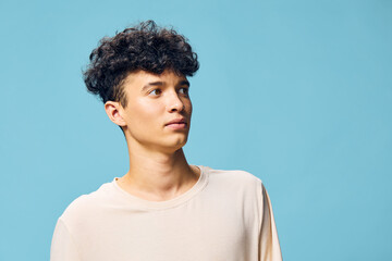 Young man with curly hair looking thoughtfully against a pale blue background, showcasing a serene and contemplative expression in a minimalist setting