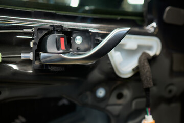 A mechanics hands are seen repairing the cars interior door panel controller inside the vehicle