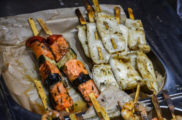 Close-up view of freshly grilled seafood skewers. Orange salmon pieces and white squid. Healthy eating, cooking, Mediterranean cuisine, or summer barbecues
