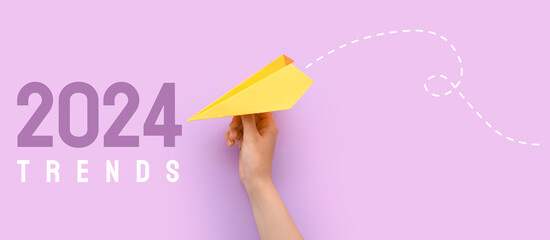 Hand with white paper plane and text 2024 TRENDS on lilac background
