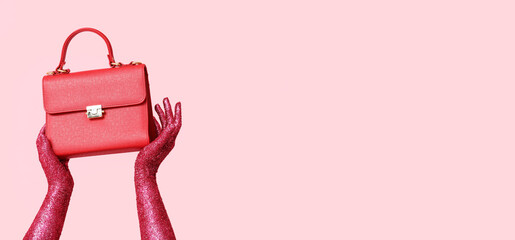 Female hands covered with glitters holding stylish handbag on pink background with space for text