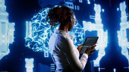 African american scientist programming scripts on tablet, employing AI machine learning infrastructure. Licensed employee manipulates lines of code for artificial intelligence applications development