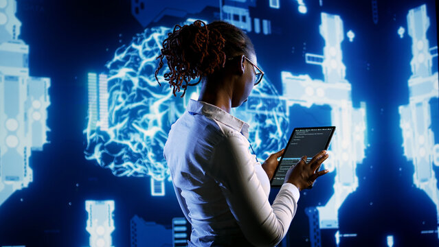 African american scientist programming scripts on tablet, employing AI machine learning infrastructure. Licensed employee manipulates lines of code for artificial intelligence applications development