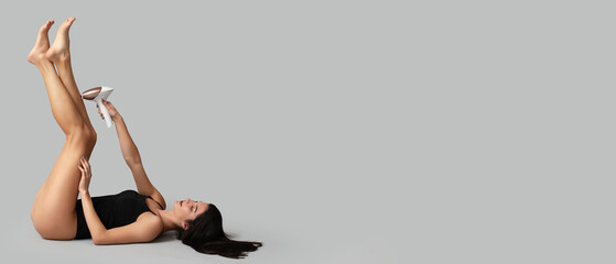 Beautiful young woman using modern photoepilator on grey background with space for text