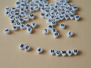Auf einem hellbraunen Untergrund liegen viele Buchstabenwürfel in Form von Herzen durcheinander, darunter bilden die Würfel eine Botschaft: BE A HUMAN