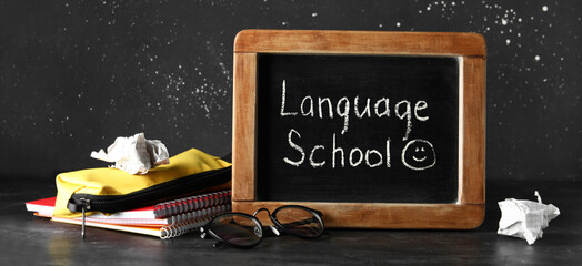 Blackboard with text LANGUAGE SCHOOL, eyeglasses and stationery on black background