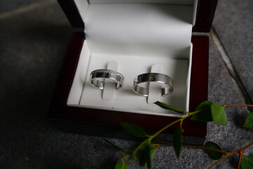 Two silver wedding rings. Women's with zircons and men's without. In a wooden box lined with white...