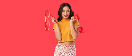 Beautiful young sexy Asian woman with whip and handcuffs on red background