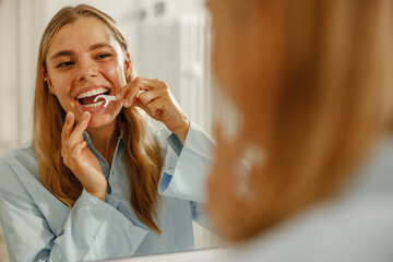 A young woman joyfully practices her dental hygiene by meticulously flossing her teeth in front of...