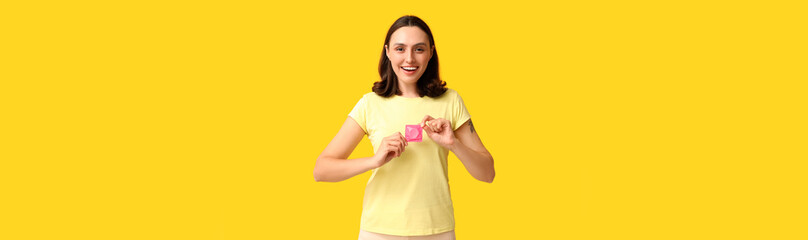 Beautiful young woman with condom on yellow background. Safe sex concept