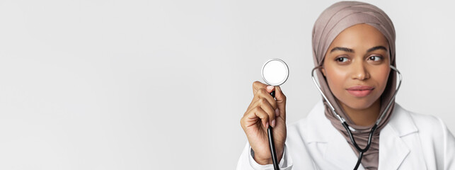 Stethoscope in hand of afro muslim female doctor in headscarf posing over light background, selective focus on arm with medical equipment, closeup