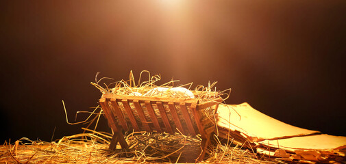 Manger with baby, hay and old book on wooden table against dark background