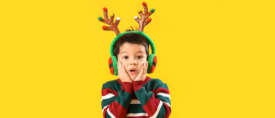 Surprised little boy in reindeer horns on yellow background