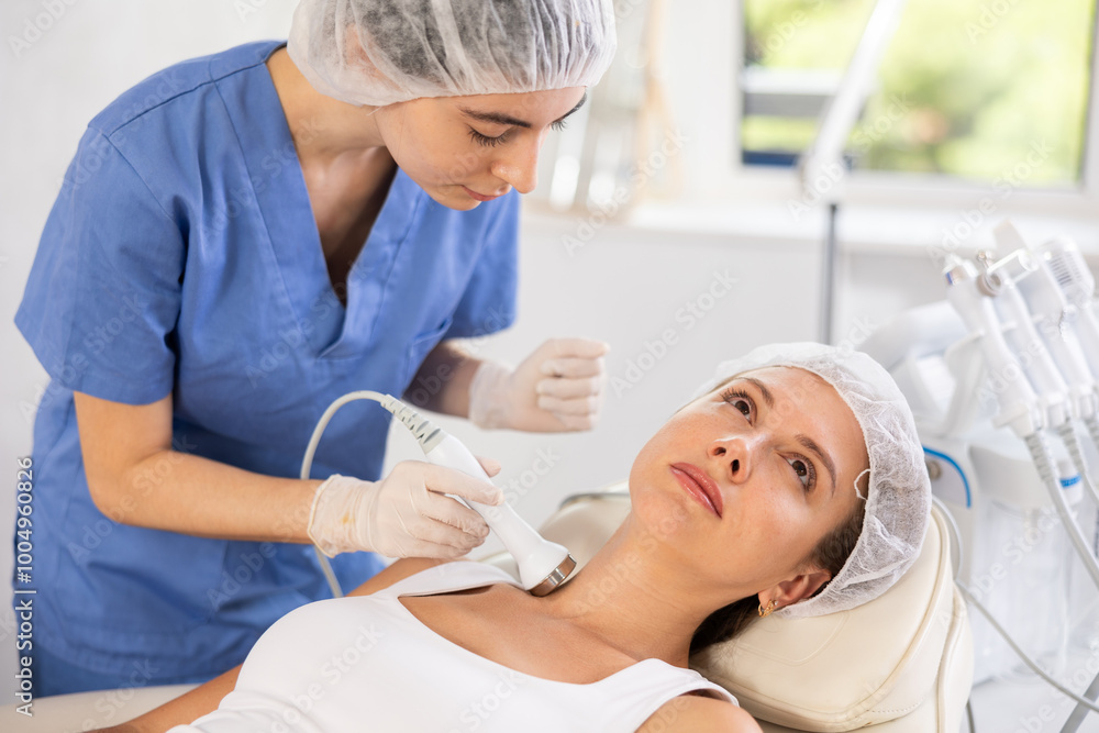 Wall mural young adult female client undergoing anti-aging ultrasonic procedure on neck at modern aesthetic med