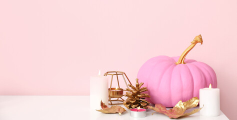 Pink painted pumpkin with autumn leaves and burning candles on white table near color wall