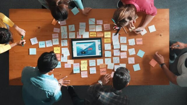 Top down view of programmer brainstorming and planning about web design while looking at tablet wireframe prototype. Aerial view of skilled developer team talking about digital application. Symposium.