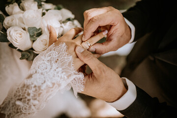 A close-up of a groom placing a wedding ring on the bride’s finger during the ceremony, with her...