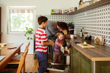 Father and children loading dishwasher together family teamwork in kitchen