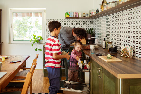 Father and children loading dishwasher together family teamwork in kitchen