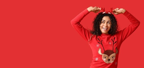 Young African-American woman in Christmas sweater and deer horns on red background with space for text