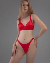 Obraz premium The model stands confidently in a vibrant red lingerie set, highlighting the smooth fabric and elegant design. The neutral background emphasizes her pose and the outfit’s details.