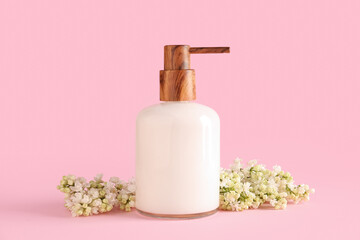 Soap dispenser with white lilac twig on pink background