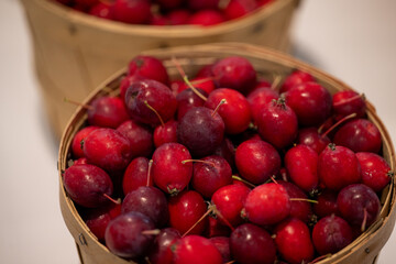 Round wooden baskets filled with fresh red cranberries. The ripe round red wild berry has thin stems attached to the fruit. The coating is waxy and shiny. The bulk berries are for sale at a market. 
