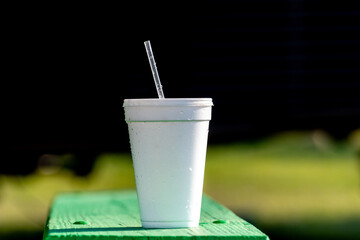 A large white nonrecyclable to-go drink cup with a plastic lid and straw on a vibrant green patio...
