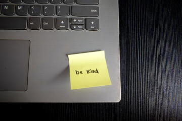 Sticky note with word Be Kind on laptop with black wood table.