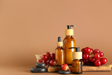 Wooden board with bottles of cosmetic products and grapes on color background
