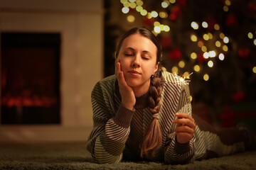 Young woman with Christmas sparkler at home in evening