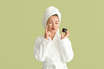 Beautiful Asian woman applying facial mask on green background