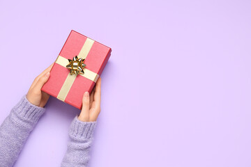 Female hands with Christmas gift on lilac background, closeup