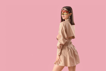 Beautiful young woman in carnival mask on pink background