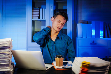 Asian businessman works late into the night, focused on a stack of papers on his black wooden desk....