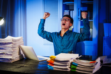 Asian businessman works late into the night, focused on a stack of papers on his black wooden desk....