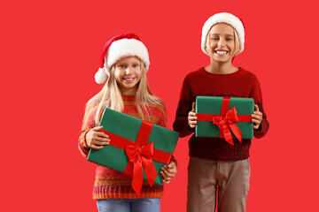 Little children in Santa hats with Christmas presents on red background