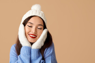 Beautiful young Asian woman in warm clothes on brown background