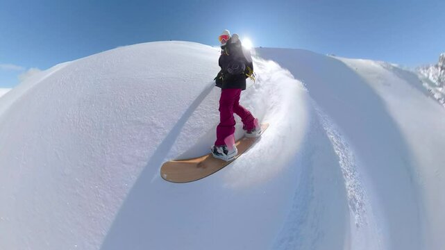 SELFIE, PORTRAIT, LENS FLARE Female snowboarder carving through pristine powder snow, leaving behind trail of fresh tracks. She genuinely enjoys stunning mountain views and snowboarding in backcountry