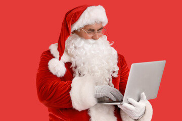 Santa Claus using laptop on red background