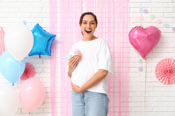 Beautiful happy pregnant woman with delicious cupcakes on white brick background. Gender reveal...