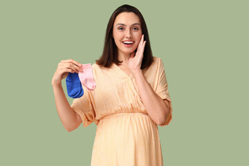 Beautiful happy pregnant woman with baby socks on green background. Gender reveal party concept