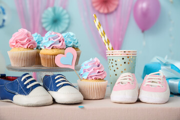 Delicious cupcakes with baby booties and decorations on table against blue background. Gender...