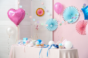 Delicious cupcakes with baby booties and decorations on table against pink background. Gender reveal party concept