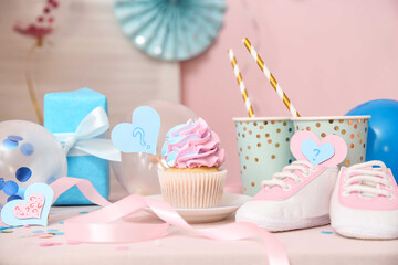 Delicious cupcake with baby booties and decorations on table against pink background. Gender reveal...