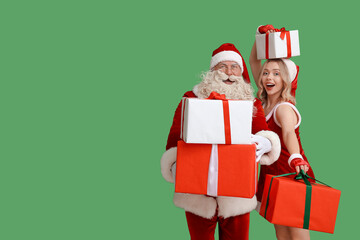 Santa Claus and beautiful young woman with Christmas gifts on green background
