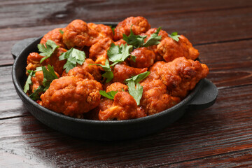 Baked cauliflower buffalo wings with parsley in baking dish on wooden table, closeup