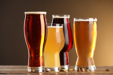 Glasses with different types of beer and pistachio nuts on wooden table against color background, closeup