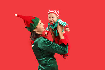 Young mother and cute little baby dressed as elves on red background